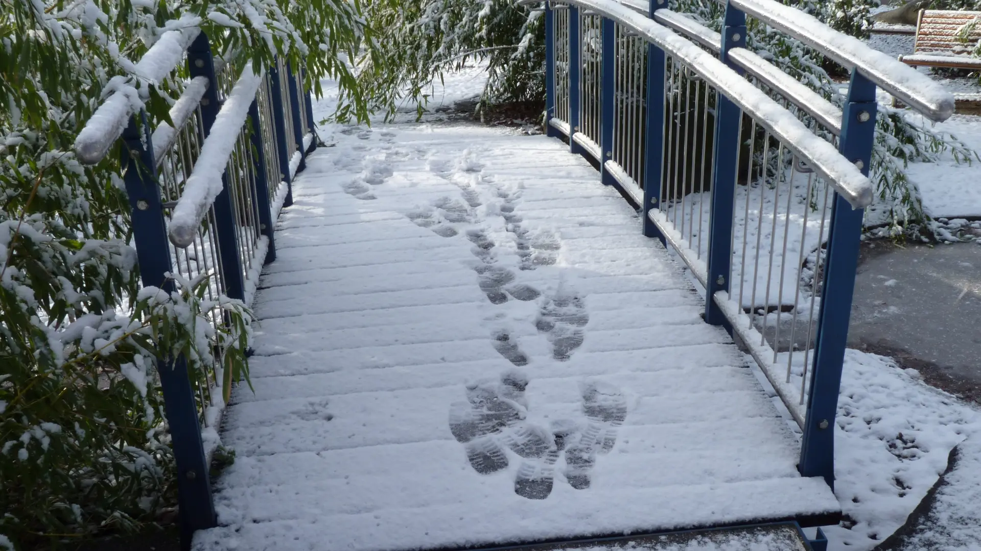 Boot prints in snow going over a bridge.