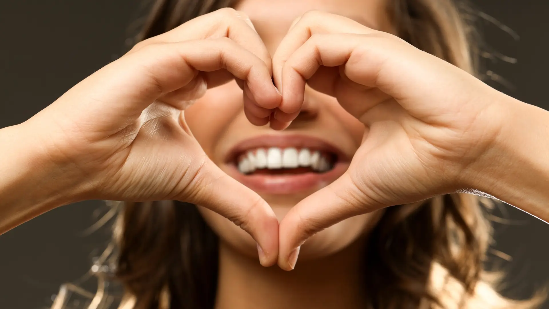 woman smiling with hands in front of her face as a heart